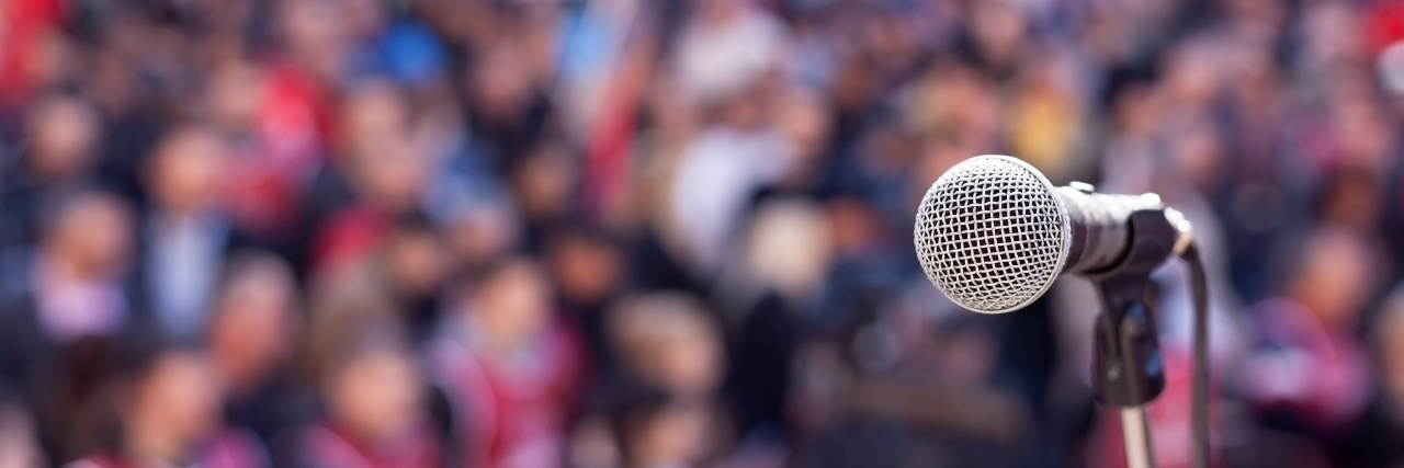 The Struggles of Being Neurodivergent in Social Justice Spaces Microphone in focus against unrecognizable crowd.