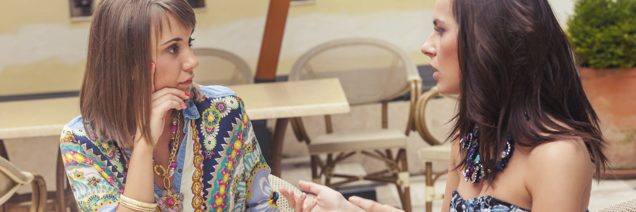Why It's Important to Ask Someone If They're Thinking About Suicide 2 women talking in a cafe. Woman on right has brown hair and colored, striped shirt. Woman on left has brown hair and is wearing a blue dress
