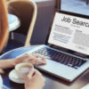 Red-haired woman holding coffee cup with hand on open laptop that reads, "Job search."