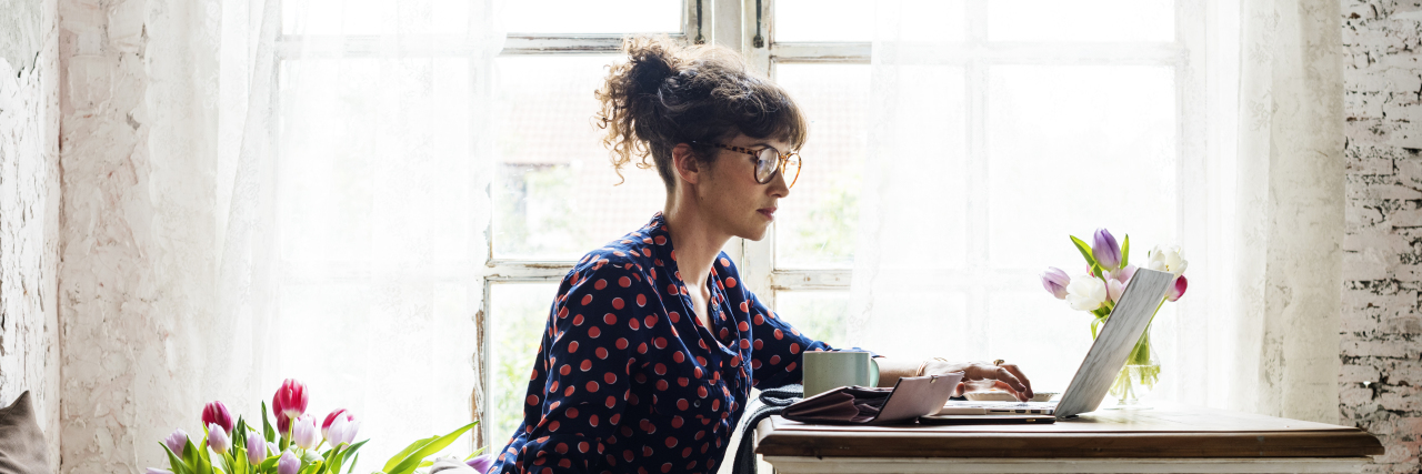 How Shopping Is Affecting My Hypomania and Sleep woman sitting on ground with flowers next to, one hand on the computer, theother petting her golden retriever