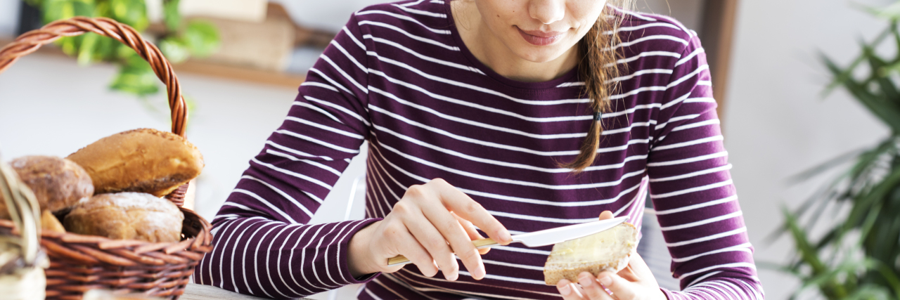 Why I Struggled to Eat a Slice of Toast in Anorexia Recovery Photo of young woman buttering slice of toast