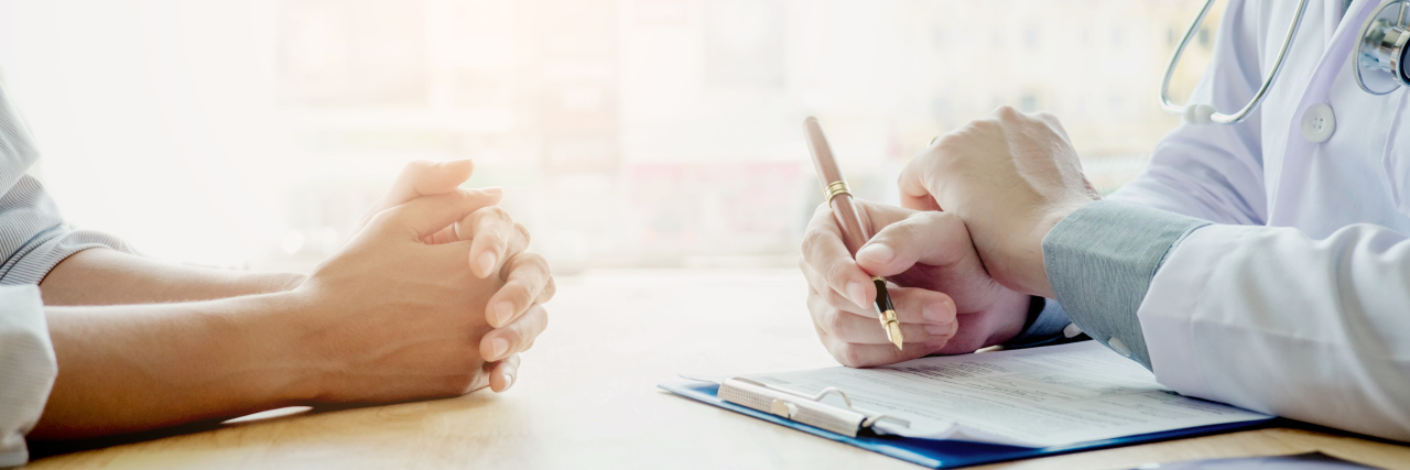 Telling New Doctors I'm in Addiction Recovery to Keep Myself Safe photo of woman discussing with doctor in consulation, bathed in golden light.