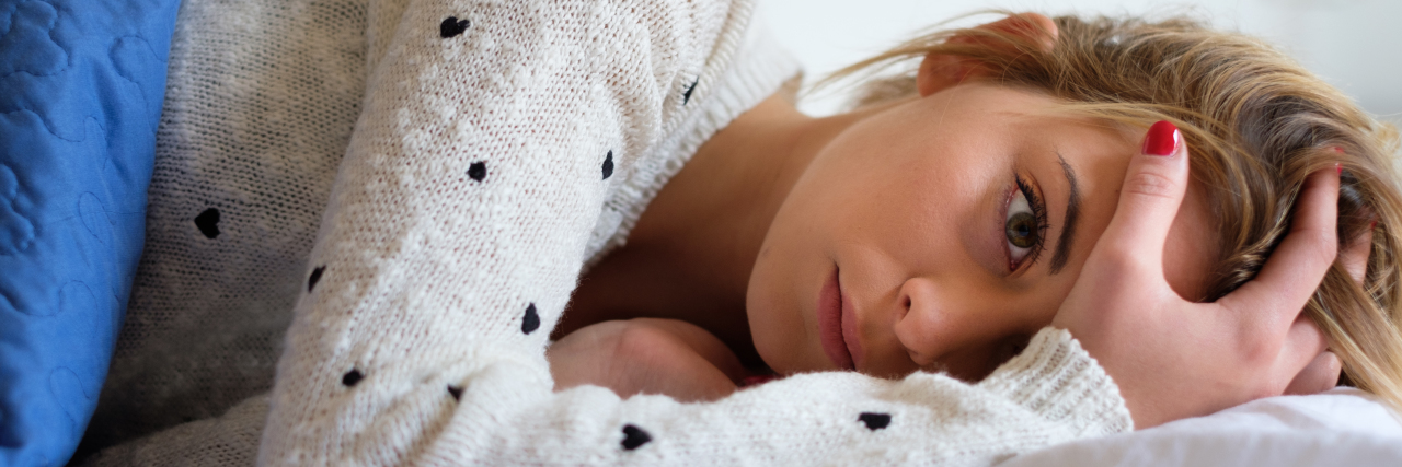 The Reality of Living With Migraine a young girl is lying on a bed holding her head