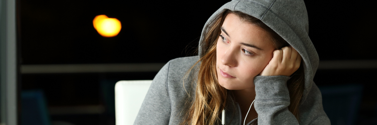 A girl sits alone with headphones in her ear, a cellphone in hand and a cup of coffee on the table.