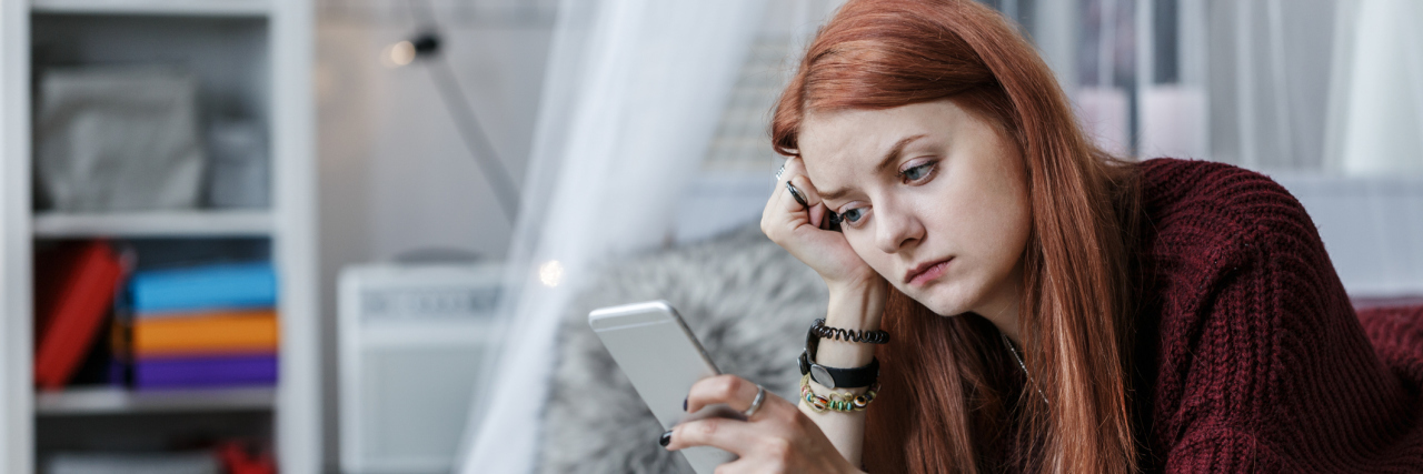 When Friends Don't Reply To My Text Messages A woman lays across a bed glancing at a cell phone.