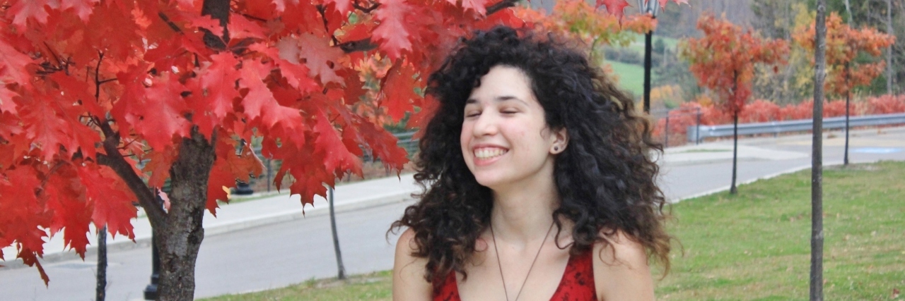 Breaking the Stigma and Raising Awareness About Narcolepsy Camille standing outside wearing a red dress, a tree with fall leaves nearby.