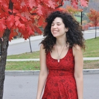 Camille standing outside wearing a red dress, a tree with fall leaves nearby.