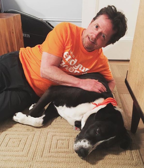 Michael J Fox wearing orange shirt while next to black and white dog