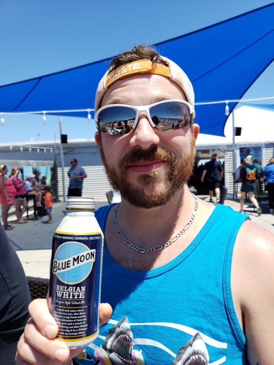 Man in sunglasses smiling holding a can of Blue Moon beer