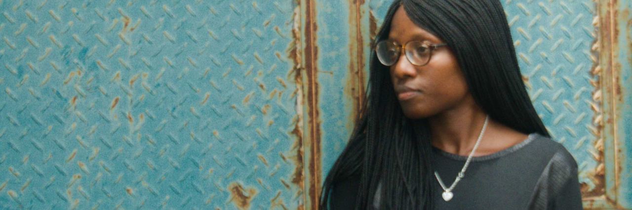 My Doctor Didn't View Me as an Individual, Just a Statistic photo of woman standing against green metal wall looking sad