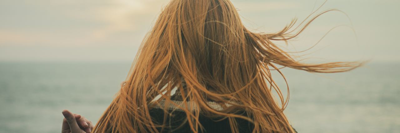 Close up picture of back of red haired woman with hair flowing looking out into the sky