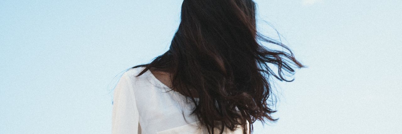 Suicide Loss Grief Makes National Suicide Prevention Week Hard photo of woman with dark hair stood against blue sky with face hidden by her hair