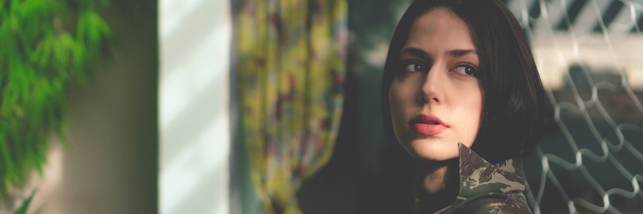 Signs of an 'Anxiety Relapse' photo of woman looking over shoulder in dim light with curtain behind her