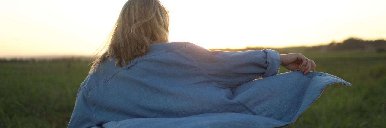 photo of blonde woman in field with window billowing shirt and sun behind her