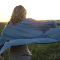 photo of blonde woman in field with window billowing shirt and sun behind her
