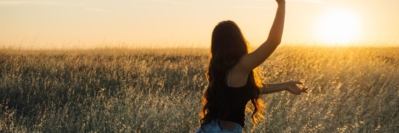 photo of woman dancing in rising or setting sun with arms stretched out, standing in field
