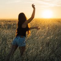 photo of woman dancing in rising or setting sun with arms stretched out, standing in field