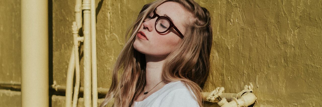 How Chronic Pain Affects Someone Throughout the Day photo of woman standing against yellow rough wall with eyes closed