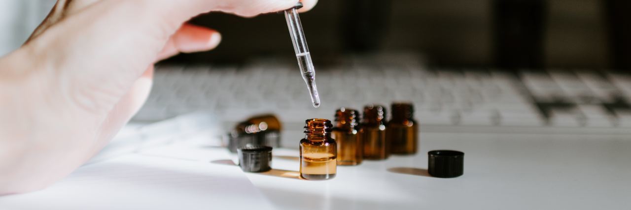 Photo of hand holding pipette extracting oil from small bottle in front of computer