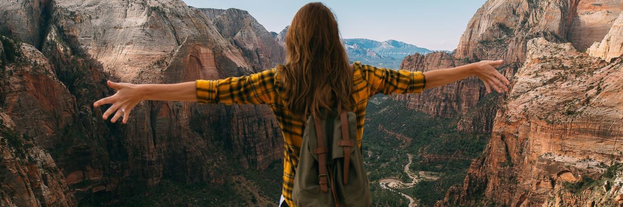 photo of young woman standing at canyon with arms outstretched to her sides