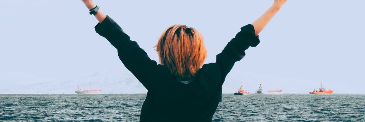 Lessons in Living After Almost Dying by Suicide photo of woman with outstretched arms by ocean with back facing camera