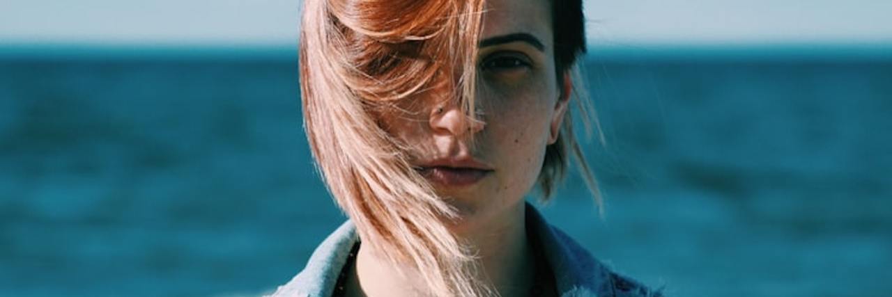 My Experience Talking About My Childhood Abuse and Neglect Close-up image of woman with red and blonde hair in a jean jacket looking at the camera with the ocean behind her