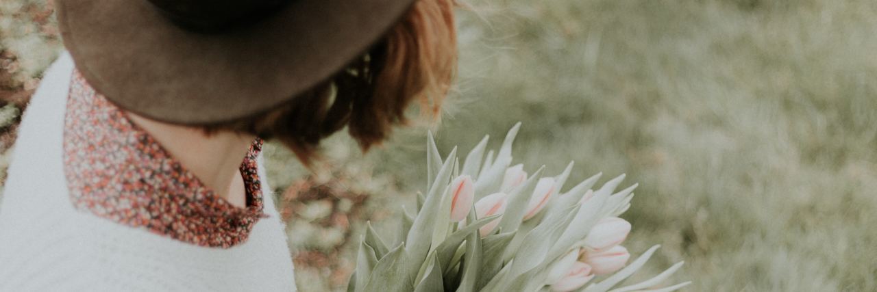 photo of woman sitting on ground wearing hat and holding flowers, looking away