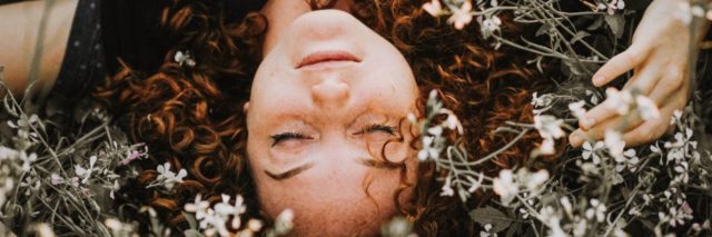 photo of redhead woman lying on ground in middle of flowers