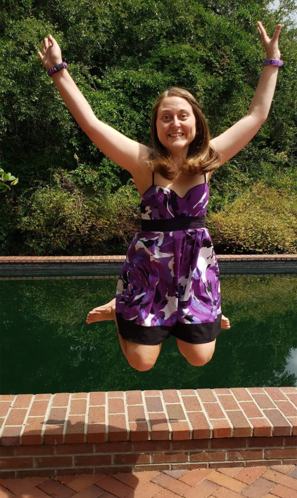 photo of contributor, Samantha Bowick, jumping into the air and smiling