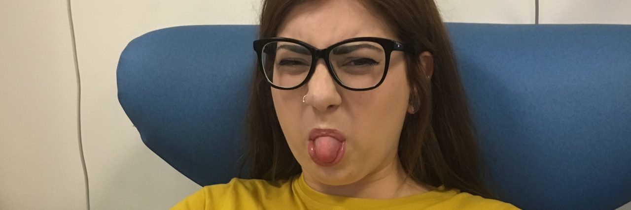 Why I Would Rather Make People Laugh About My Illness sophie sitting in a chair at doctor's office sticking her tongue out