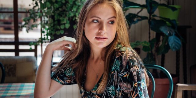 4 Reasons the ‘Sober Curious’ Movement Could Harm People Living With Addiction photo of woman in restaurant looking back over shoulder with elbow resting on table