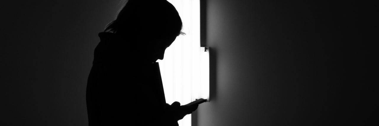 Smartphone Addiction, Anxiety and How to Deal With It black and white photo of woman looking at smartphone with abstract bright light behind her