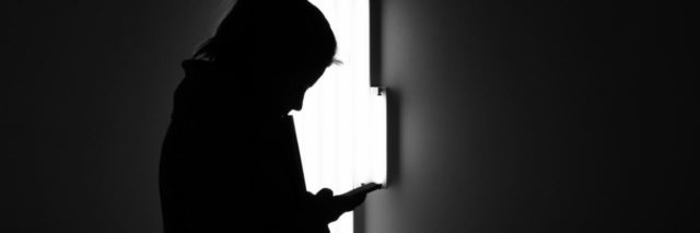 black and white photo of woman looking at smartphone with abstract bright light behind her