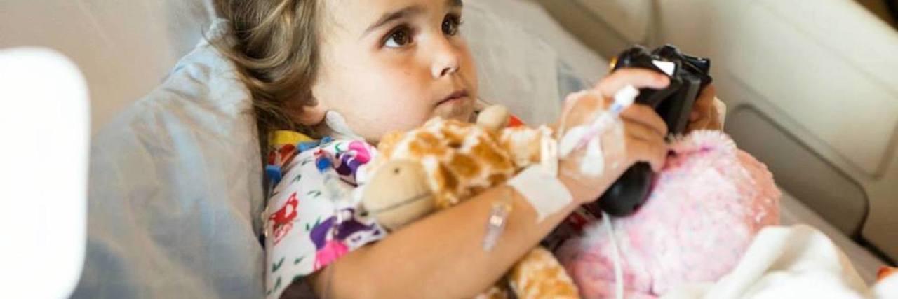 The Never-Ending Battle for My Daughter's Transplant Medications A girl in a hospital bed playing a video game