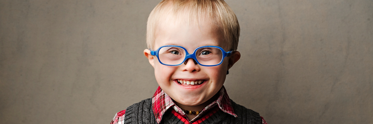 Photo Series Shatters Down Syndrome Myths Kat's son, a boy with Down syndrome wearing blue glasses and a sweater vest.
