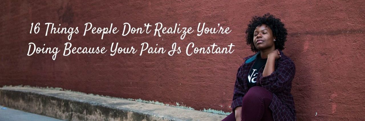 Things People Don’t Realize You’re Doing Because You Pain Is Constant woman with black top and purple pants sitting on the street with back against the wall grabbing at neck