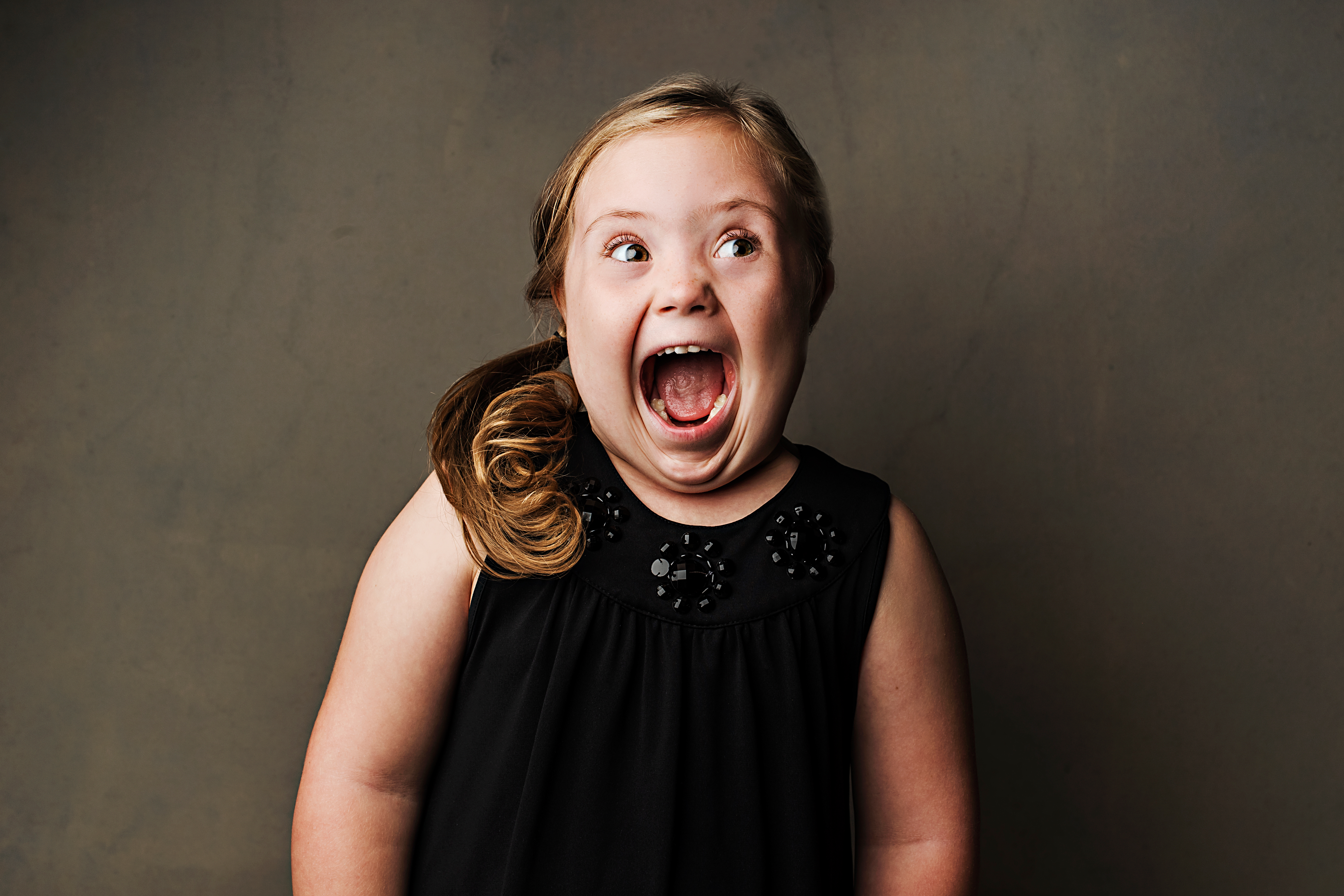 Joyful girl with Down syndrome, wearing a black dress.