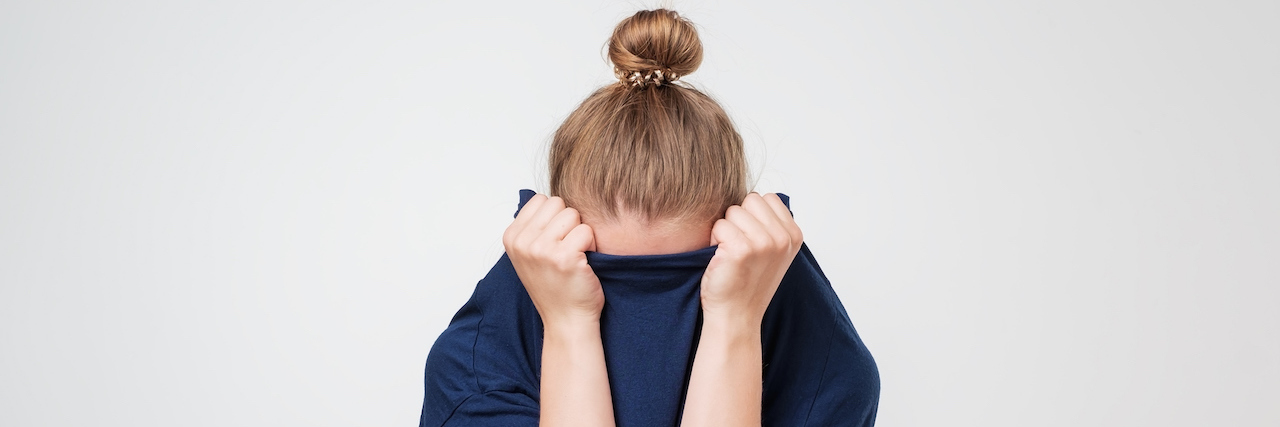 woman hiding face under her clothes.