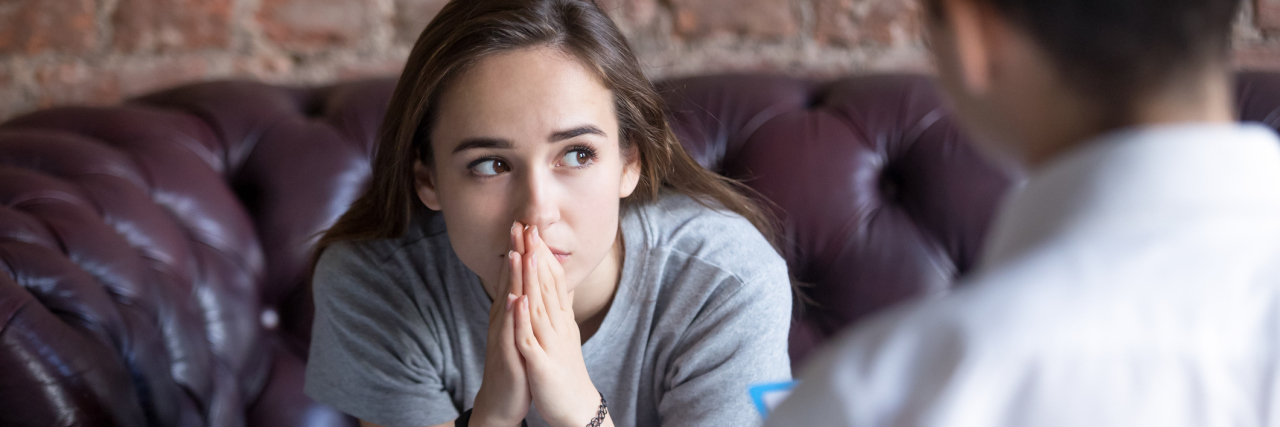 What I Learned From Being in a Psychiatric Hospital A woman sits with her hands together speaking to a medical professional.