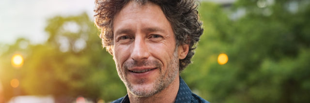 A man with curly greyish hair smiling outside