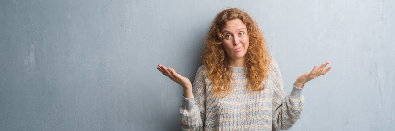 Reasons Why People Don't Believe in Mental Illness woman with long curly read hair in a striped white and grey sweater confused with her hands up