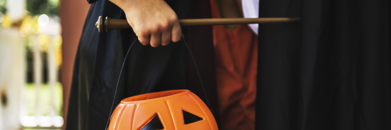 A child dressed as a witch holding a pumpkin shaped trick or treating bag