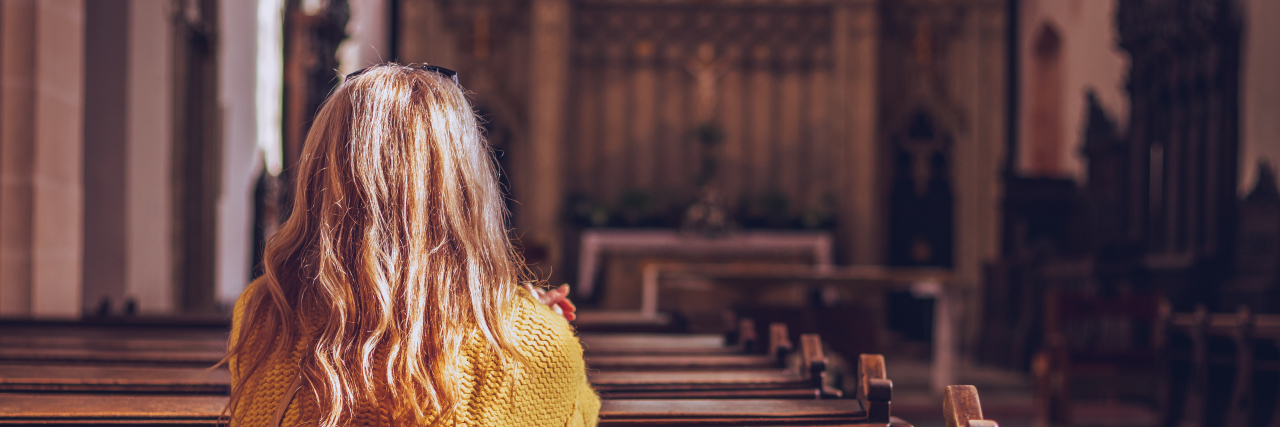 Woman in yellow sweater and blonde hair sitting in a pew at church praying