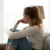 side view of a woman in jeans a long sleeve white shirt sitting on a couch looking out the window