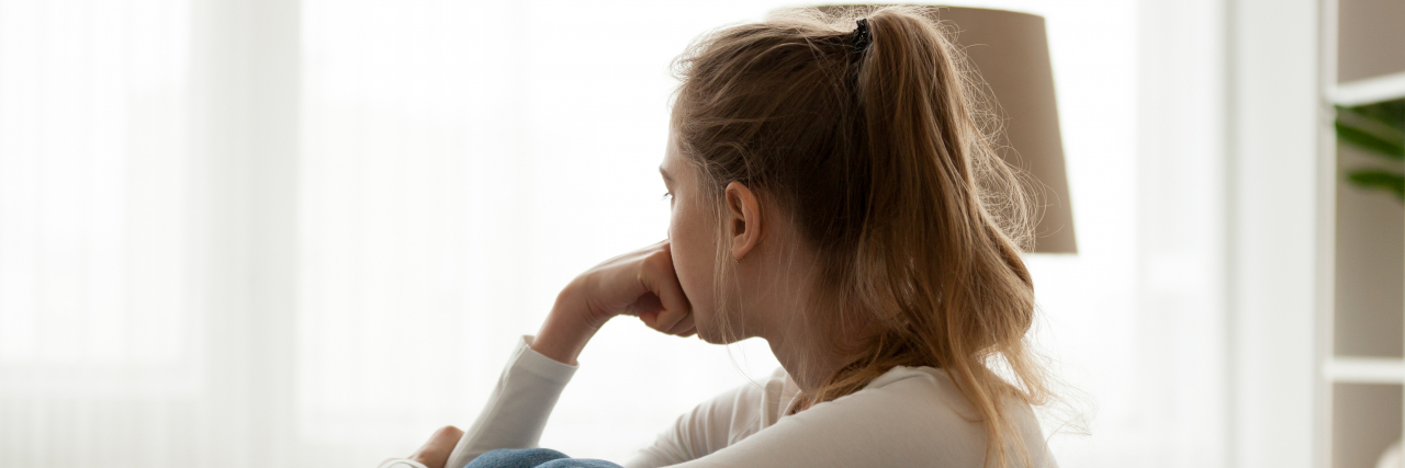 Finding Balance Between Routines and Novelty When You Live With Autism and ADHD side view of a woman in jeans a long sleeve white shirt sitting on a couch looking out the window
