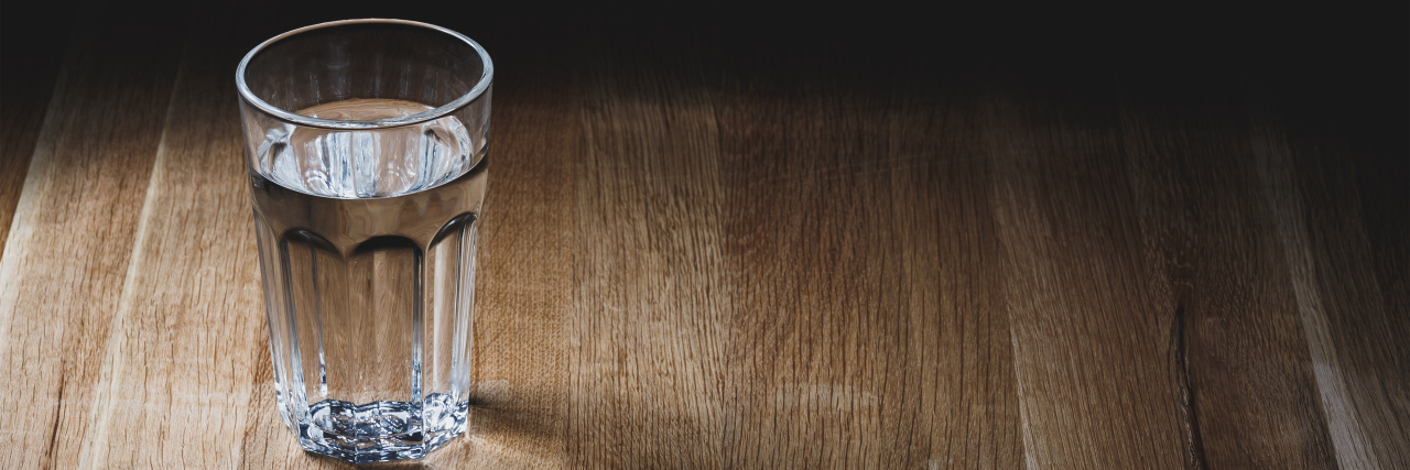 Attending Graduate School With Chronic Illness Glass of water on wood table surface.