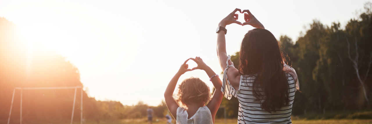 Mother and daughter making hearts with their hands.