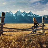 Woman sitting on a fence looking at mountains.