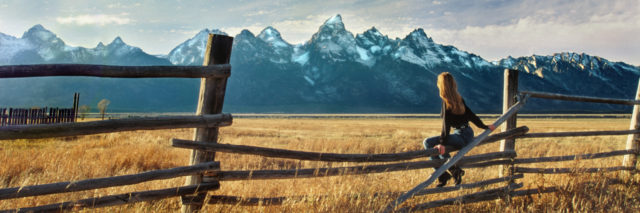 Woman sitting on a fence looking at mountains.