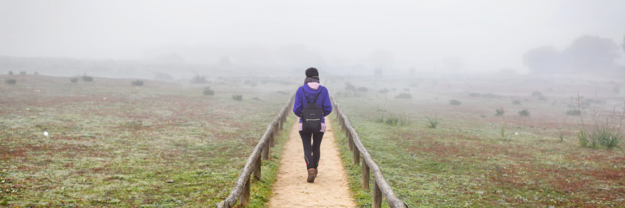 Living With an Incurable Illness: What it Feels Like woman walking alone on a field surrounded by fog.